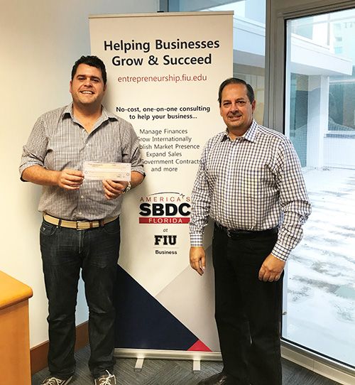 Eric Maradiaga, owner of Titan Lumber, receiving his disaster assistance check from SBDC at FIU consultant Julio Villiers